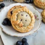 Blueberry lemon mini pies on a plate surrounded by more pies and fresh blueberries.
