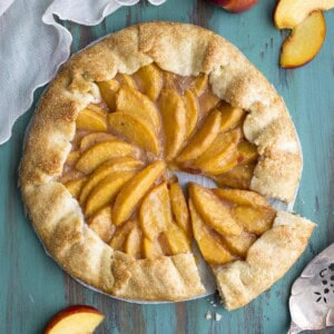A peach galette on a green table top, a slice is cut out.