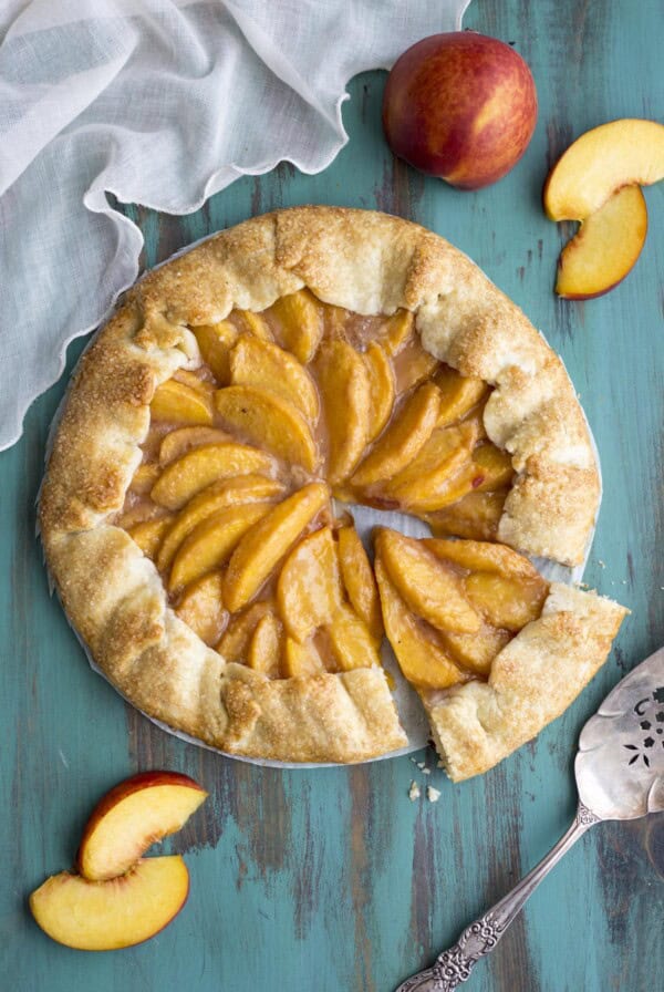 A peach galette on a green table top, a slice is cut out.