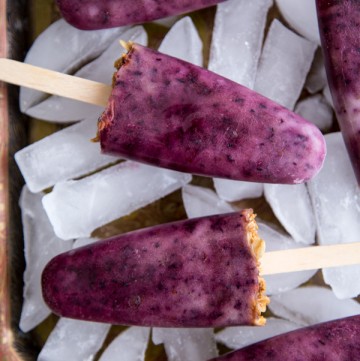 Blueberry Popsicles laying on top of ice cubes on a tray
