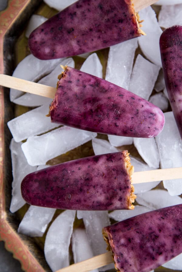 Blueberry Popsicles laying on top of ice cubes on a tray