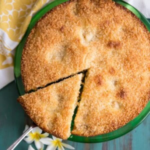 A slice of mango coconut cake is cut out of the whole cake on a green plate.