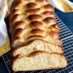 A loaf of Challah bread with two loose slices on a wire rack.