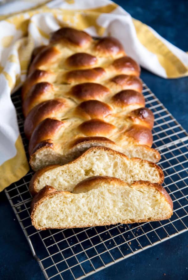 A loaf of Challah bread with two loose slices on a wire rack.