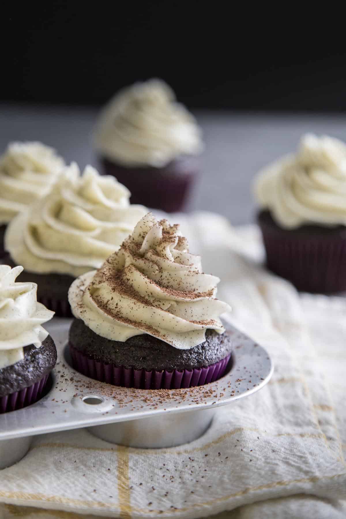 Chocolate cupcakes with vanilla frosting and chocolate dusting in a muffin pan.