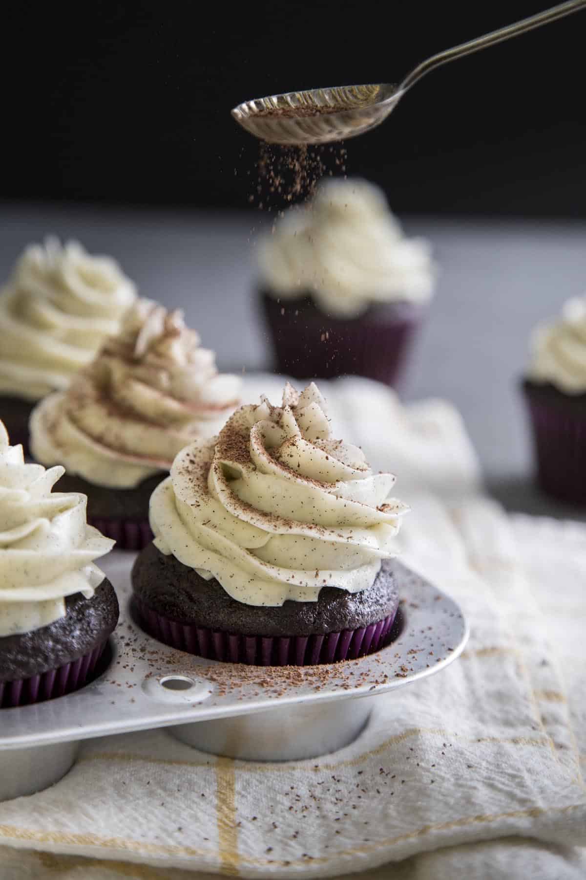 Sprinkling chocolate shaving over chocolate cupcakes with swiss meringue buttercream