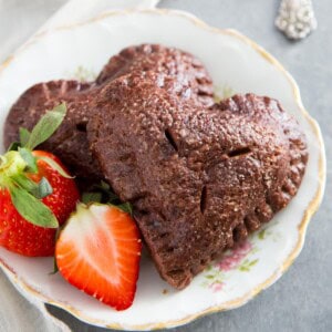 Heart shape chocolate strawberry hand pies on a plate with strawberries.