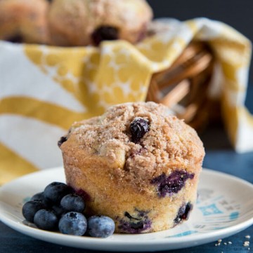 Blueberry muffin on a plate with fresh blueberries scattered around