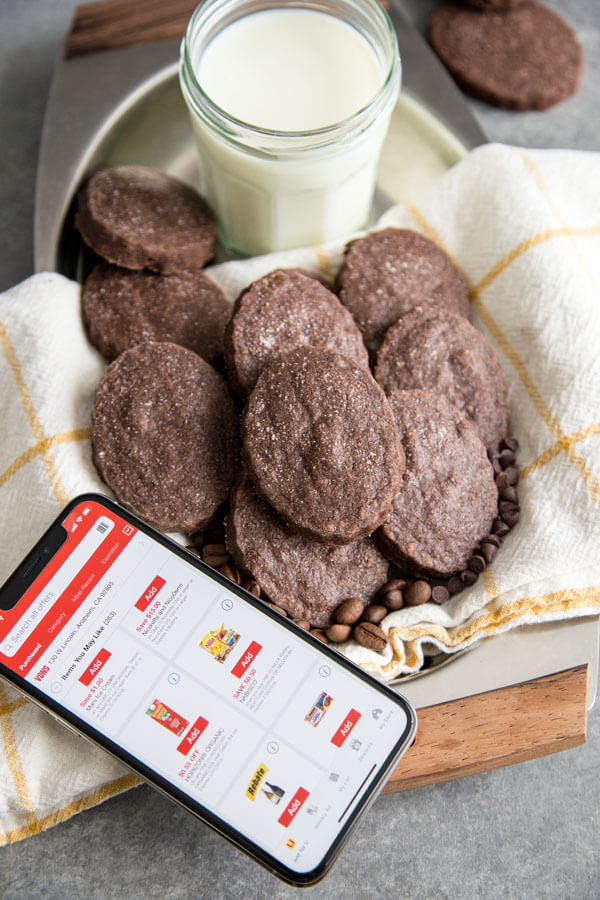 Chocolate Espresso Shortbread Cookies on a serving tray next to a glass of milk and a phone open to a coupon page