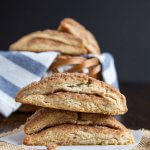 A stack of two cinnamon scones on a table and a basket of scones in the background