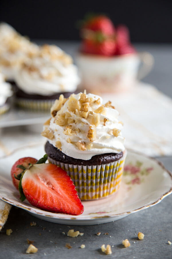 A banana split cupcake on a plate with a strawberry