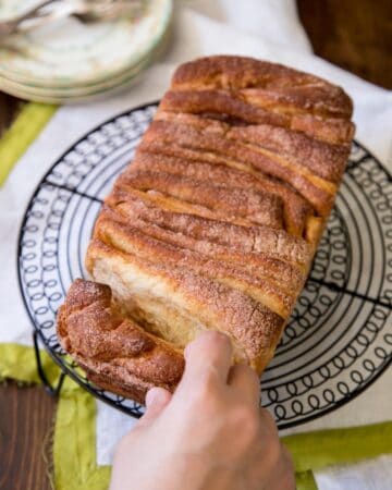 Cinnamon pull apart bread on a round wire rack being pulled apart.