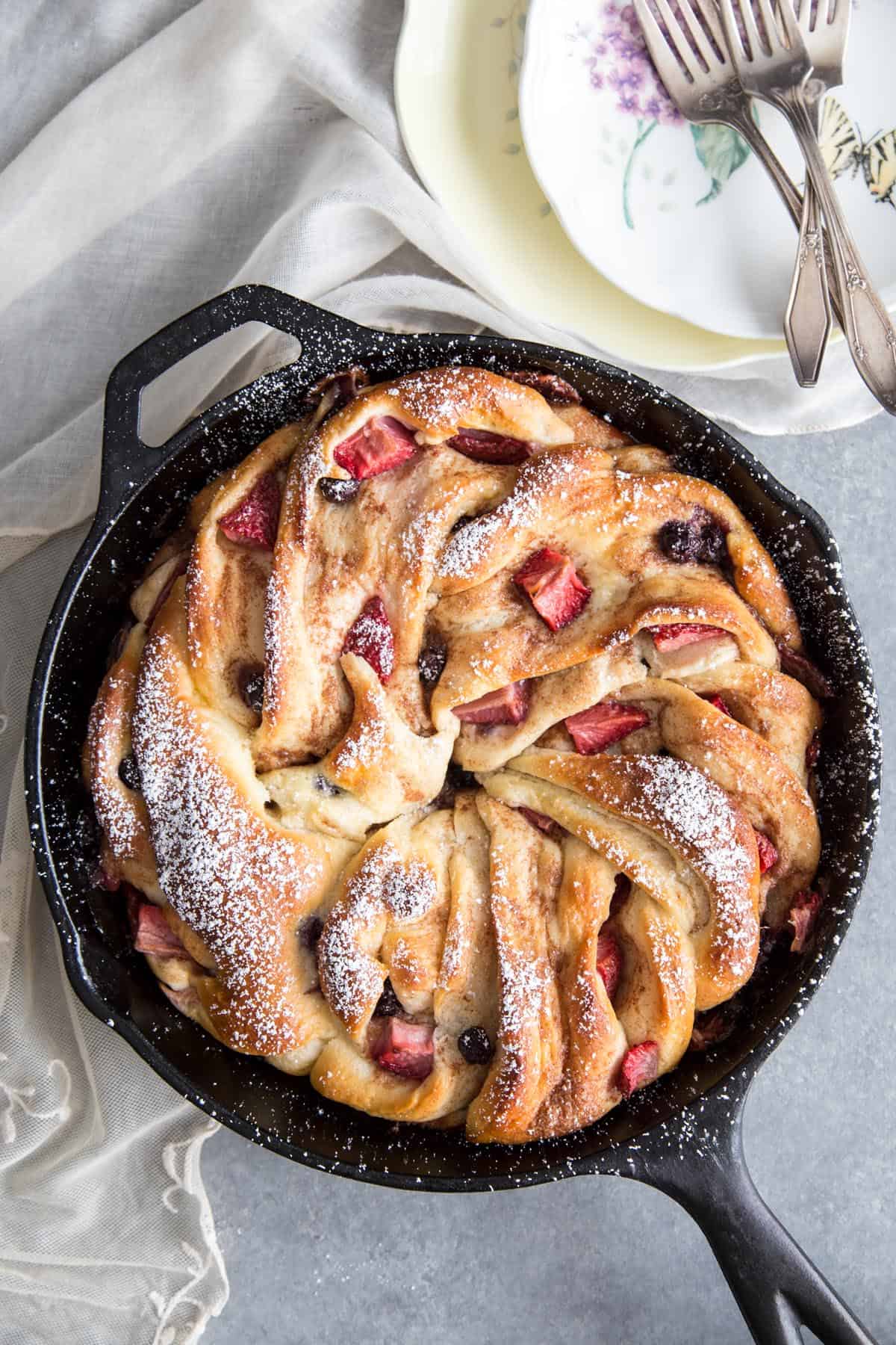 Braided cinnamon bread with berries in a cast iron pan.