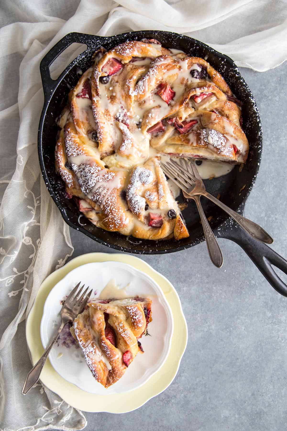 Cinnamon swirl bread in a cast iron skillet next to a slice of bread on a plate.