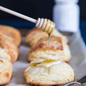 Honey buttermilk biscuits on a cooling rack being drizzled with honey