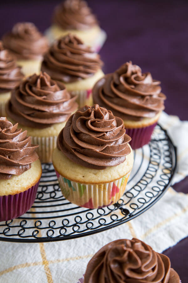 Vanilla cupcakes with chocolate frosting on a round wire rack