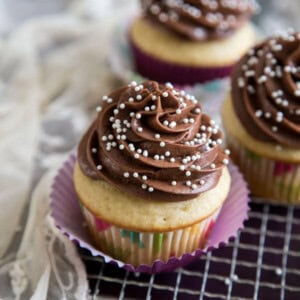 Vanilla cupcakes with chocolate frosting and sugar pearl decoration on a metal rack