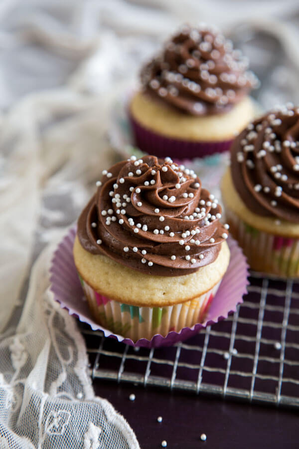 Vanilla cupcakes with chocolate frosting and sugar pearl decoration on a metal rack