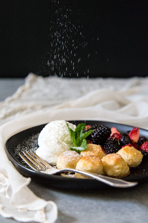 Deconstructed berries and cream shortcake on a plate being sprinkled with caramel dust