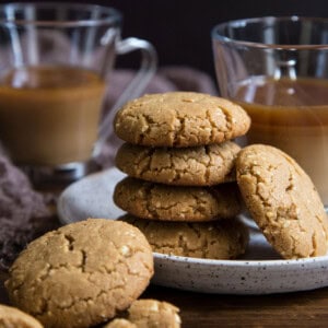 A stack of brown butter peanut butter cookies on a plate with two glasses of coffee.