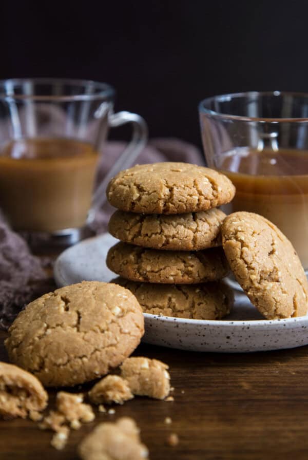 A stack of brown butter peanut butter cookies on a plate with two glasses of coffee.