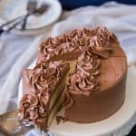 A slice of yellow cake with chocolate frosting on a white cake stand being lifted up by a cake server