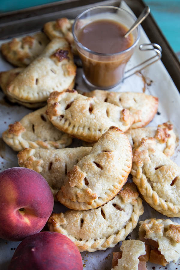 A pile of peach hand pies on a baking sheet