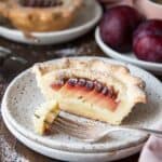 A mini plum tart cut in half on a plate with another tart in the background.