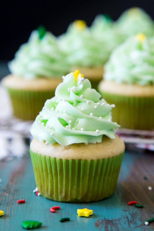 A pretty Christmas Cupcake with mint buttercream sitting on a green surface, more cupcakes are in the background.