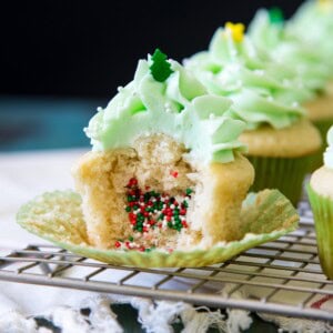 A half eaten piñata cupcakes with Christmas sprinkles spilling out of it.