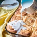 Pouring coconut sauce over baked tropical cinnamon rolls.