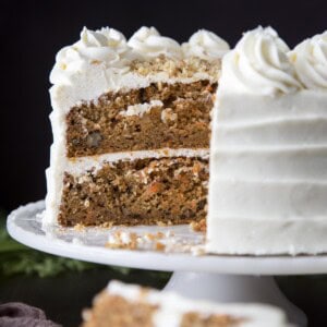 Carrot cake on a cake stand with slices cut away showing the interior.