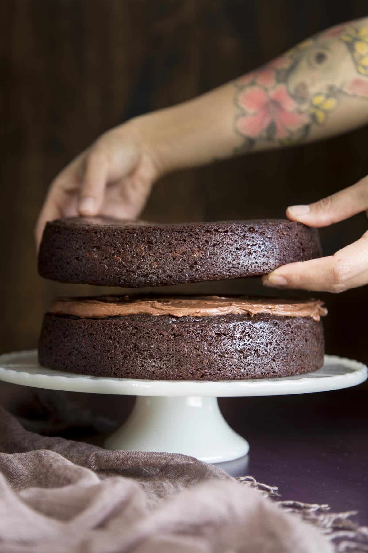 Assembling chocolate cake with a layer of chocolate frosting.