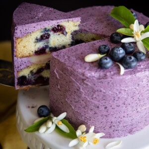 A small blueberry lemon cake with a slice cut out being served.