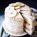 An apple pie cake on a cake stand with a slice being served.
