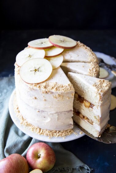 An apple pie cake on a cake stand with a slice being served.