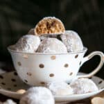 Snowball cookies in a tea cup with one half eaten cookie at top.