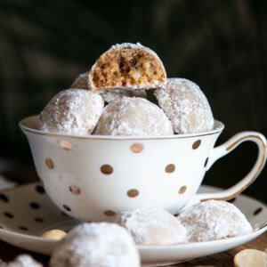 Snowball cookies in a tea cup with one half eaten cookie at top.