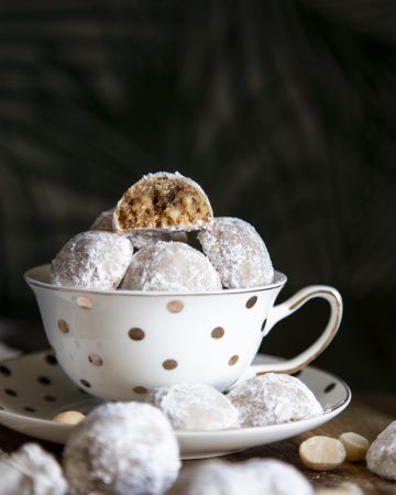 Snowball cookies in a tea cup with one half eaten cookie at top