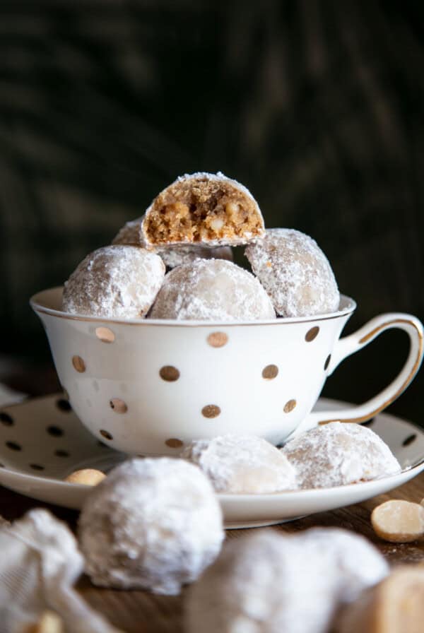 Snowball cookies in a tea cup with one half eaten cookie at top.