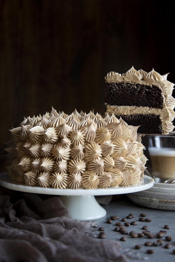 A slice of mocha cake is being lifted up from the whole cake on a cake stand.