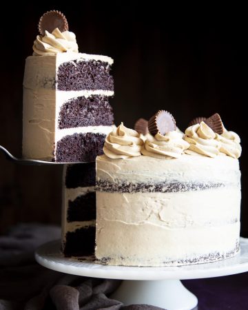 A slice of chocolate cake covered in peanut butter frosting is being lifted off the cake stand with the whole cake