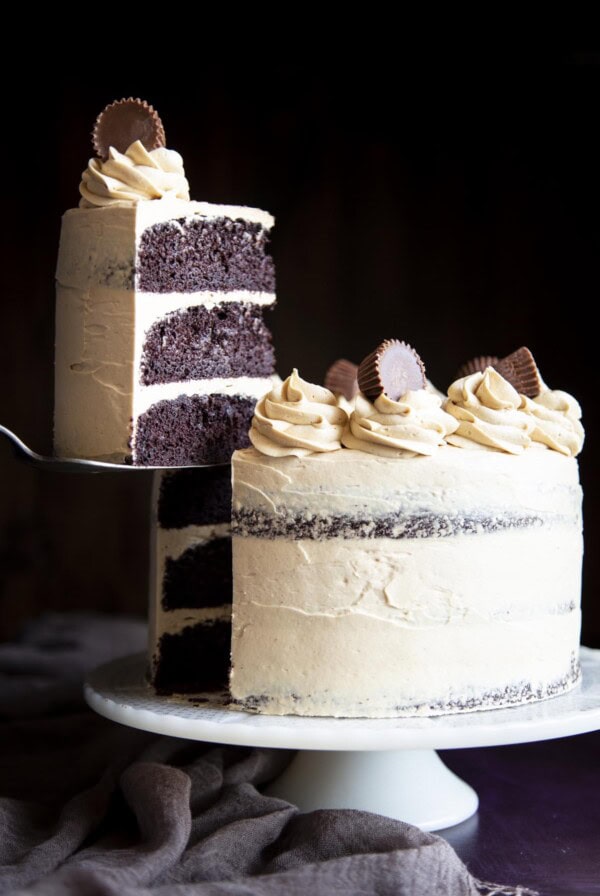 A slice of chocolate cake covered in peanut butter frosting is being lifted off the cake stand with the whole cake