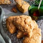 A pile of scones on a glass plate with a green tea cup, more scones in the background.
