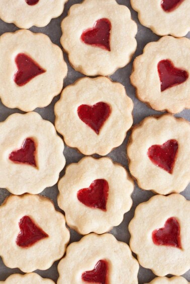 Stained glass cookies with heart shaped candy in the middles laying flat on a grey surface