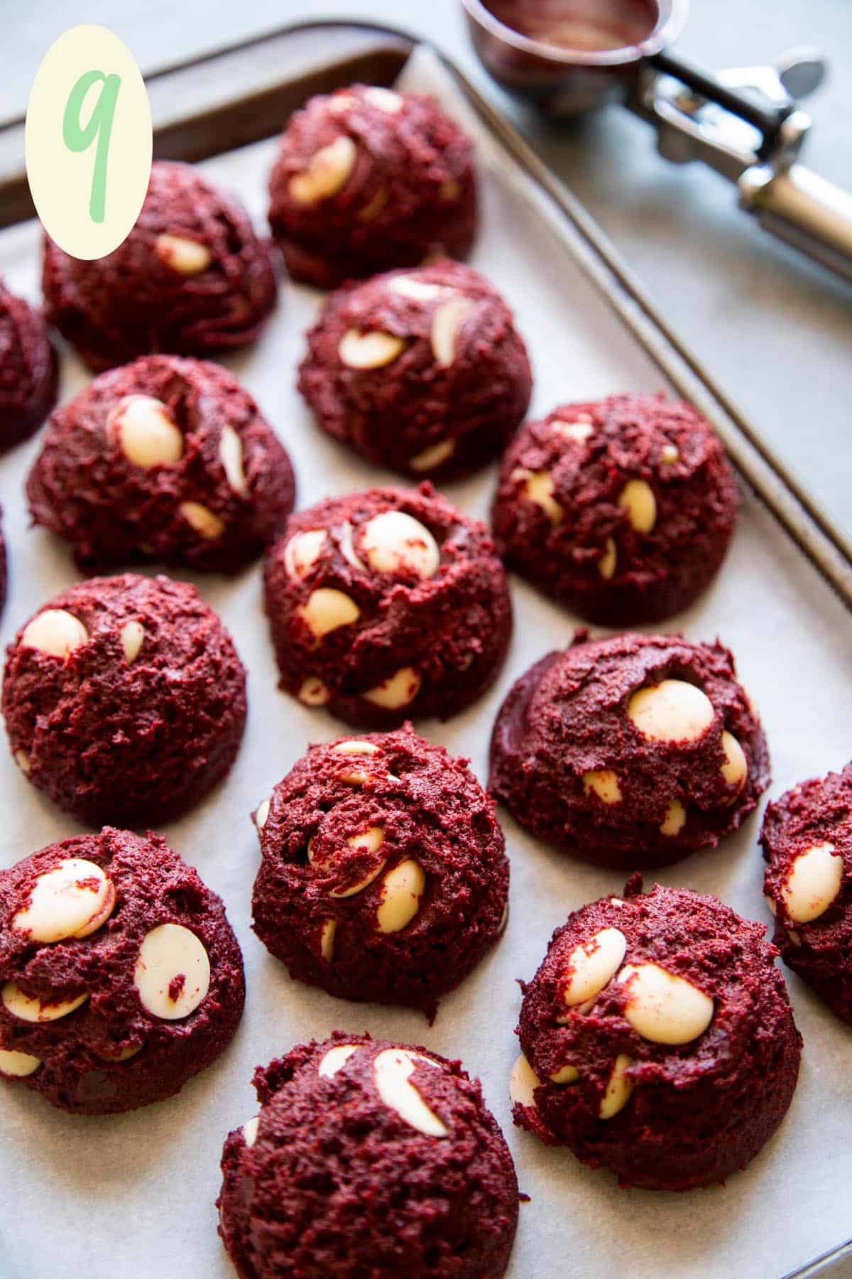 Red velvet cookie dough balls with white chocolate on a lined baking sheet