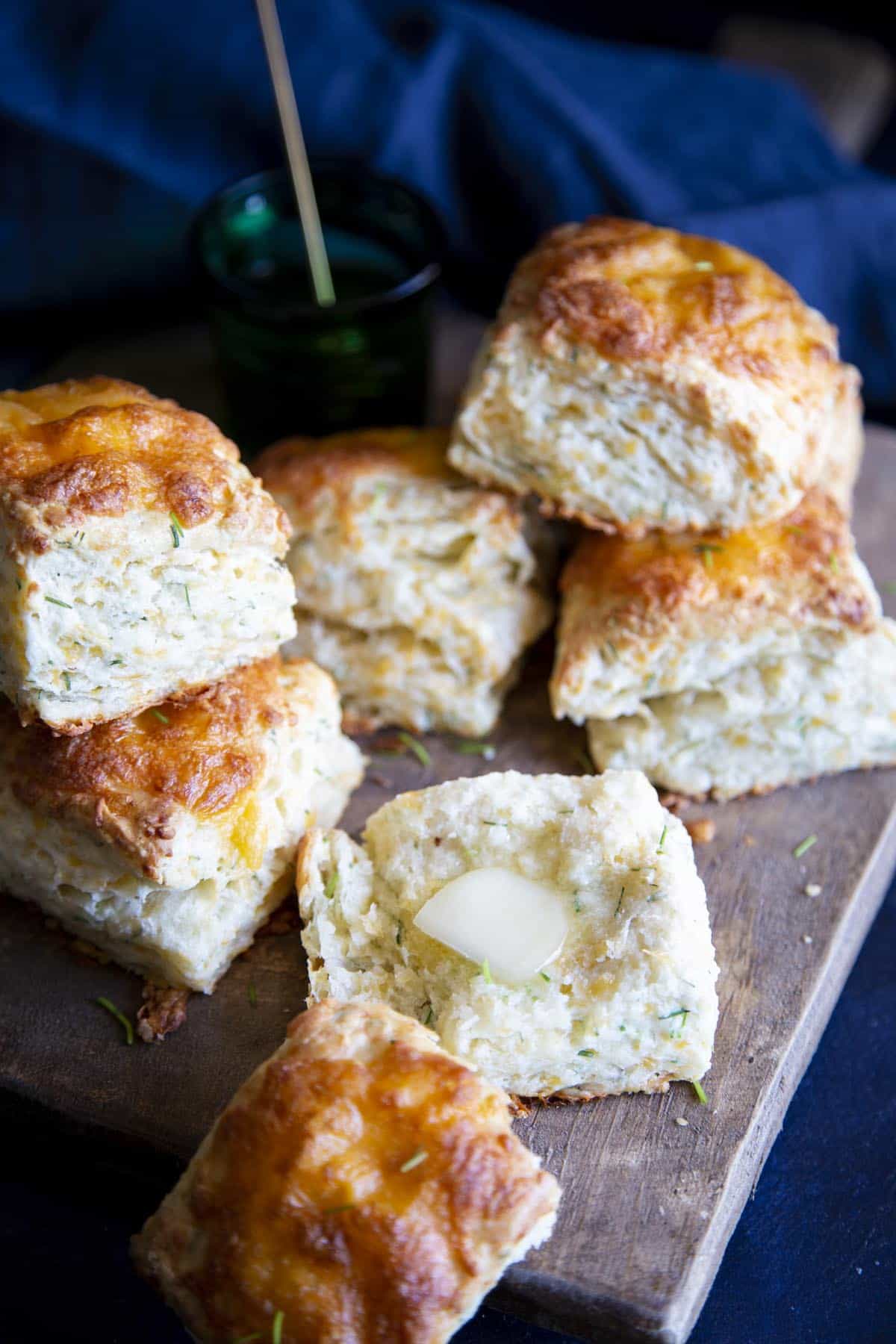 Flaky and Fluffy Cheese Biscuits with Chives Cheese biscuits on a wooden board, one is broken open with a pat of butter on it.