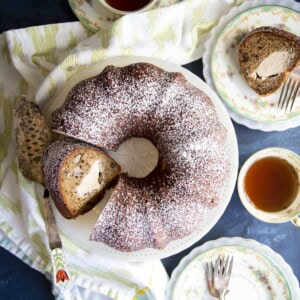 A sliced banana bundt cake on a cake stand, with tea and cake slice on plates surrounding it.