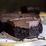 A slice a chocolate cake with chocolate ganache with a fork in front.