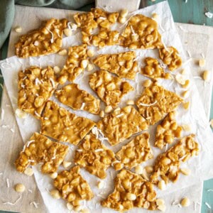 Pieces of macadamia brittle on a white wooden board.